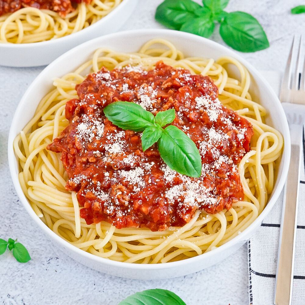 Kom met spaghetti met rode saus, bestrooid met Parmezaan en basilicumblaadjes op lichte tafel.